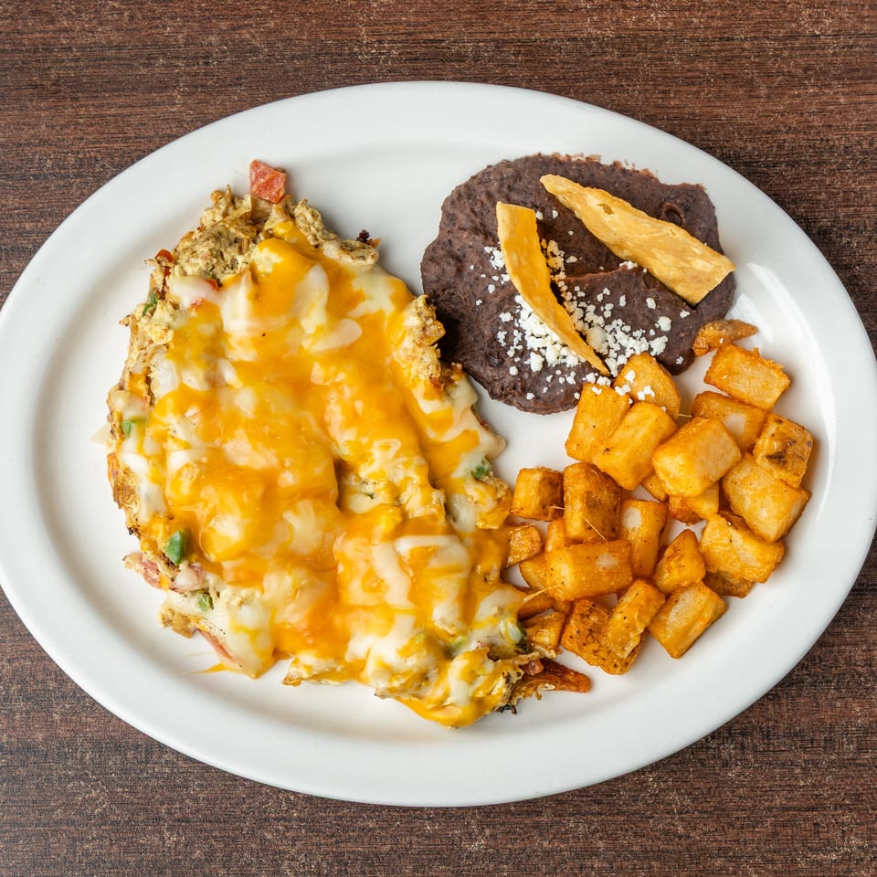 A cheesy omelet with home fries and refried beans on a white plate.