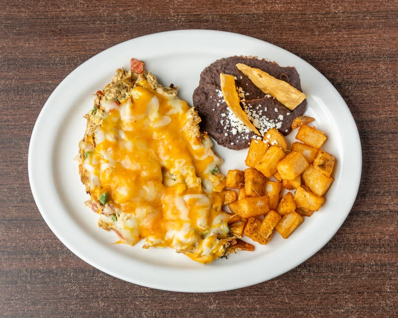 A cheesy omelet with home fries and refried beans on a white plate.