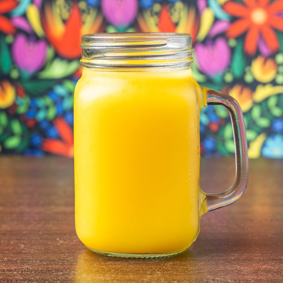 A mason jar mug filled with a bright yellow drink sits on a wooden table.