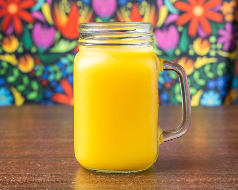 A mason jar mug filled with a bright yellow drink sits on a wooden table.