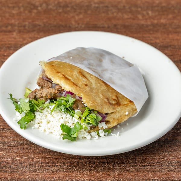 Arepa filled with meat, red onions, cilantro, and crumbled white cheese on a white plate.